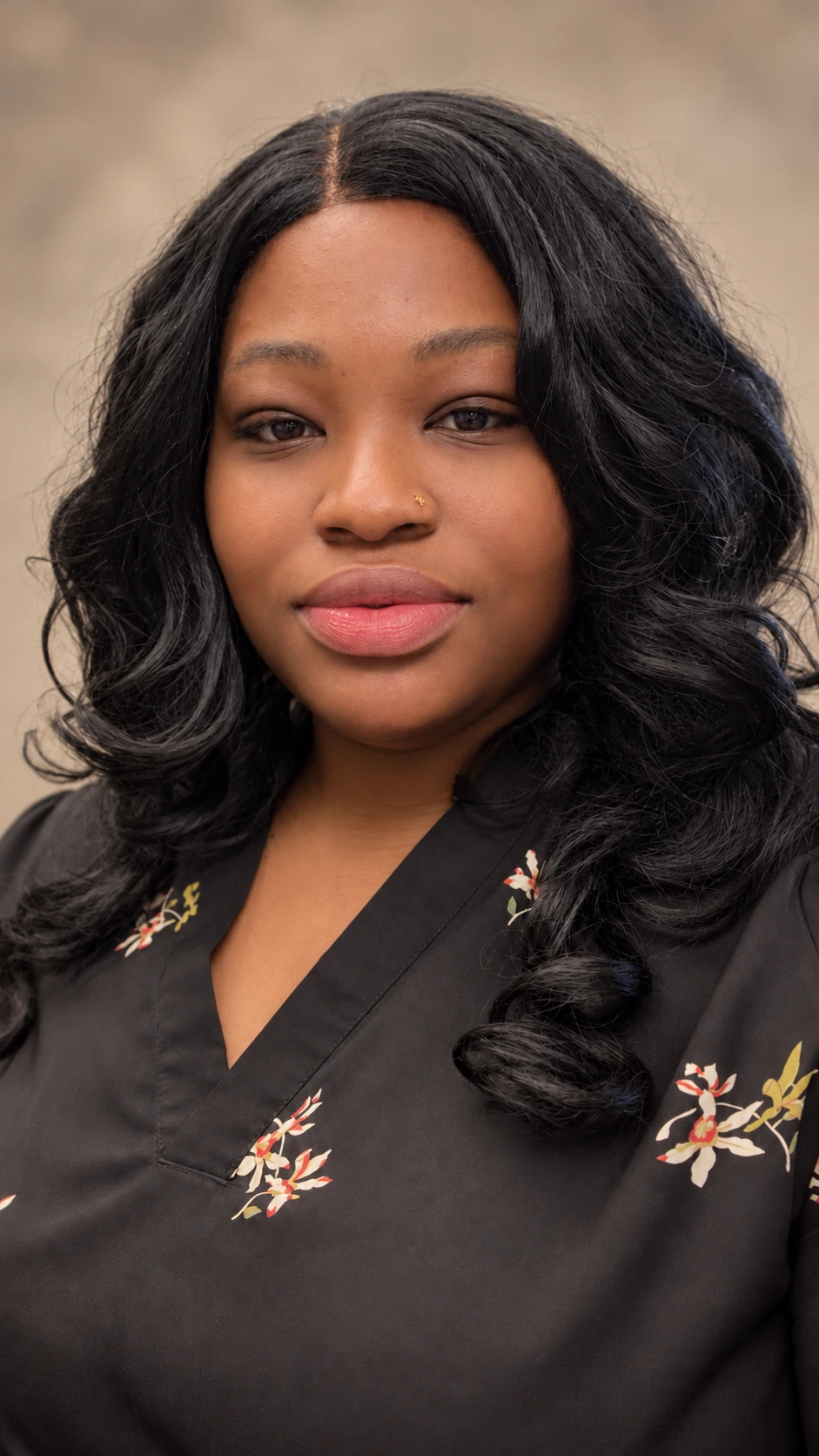 Professional portrait of Nordia McNish wearing a black floral blouse against a warm neutral background
